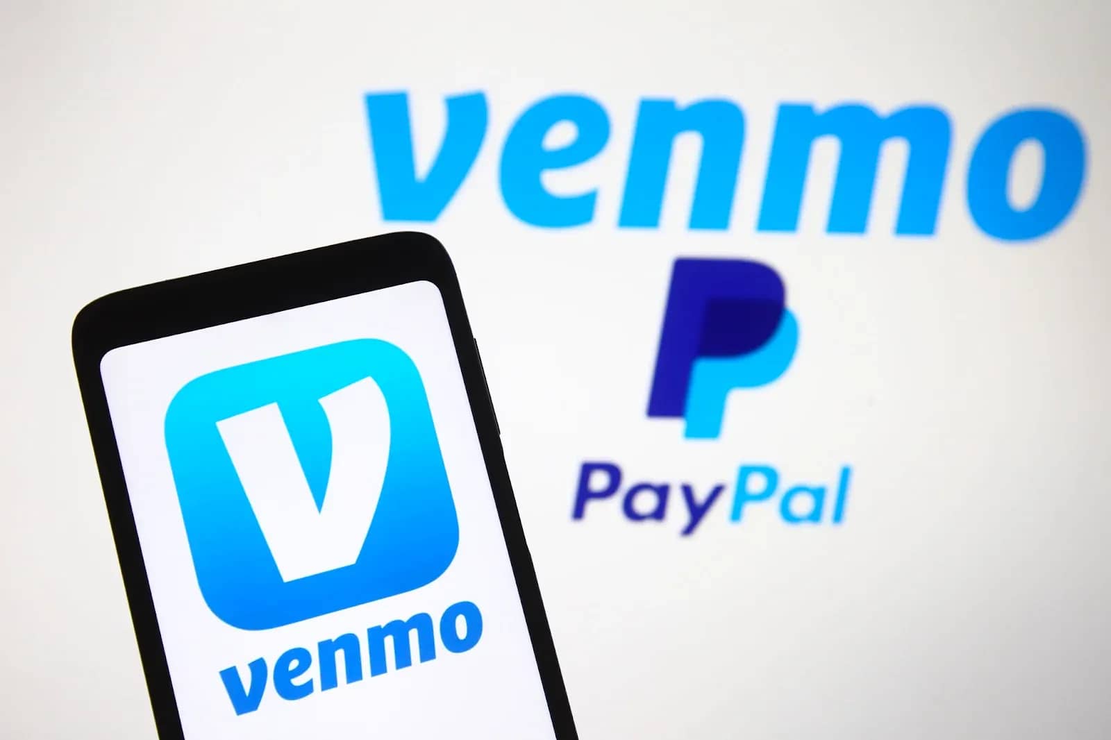 Venmo app icon on a phone in front of the Venmo and PayPal logos