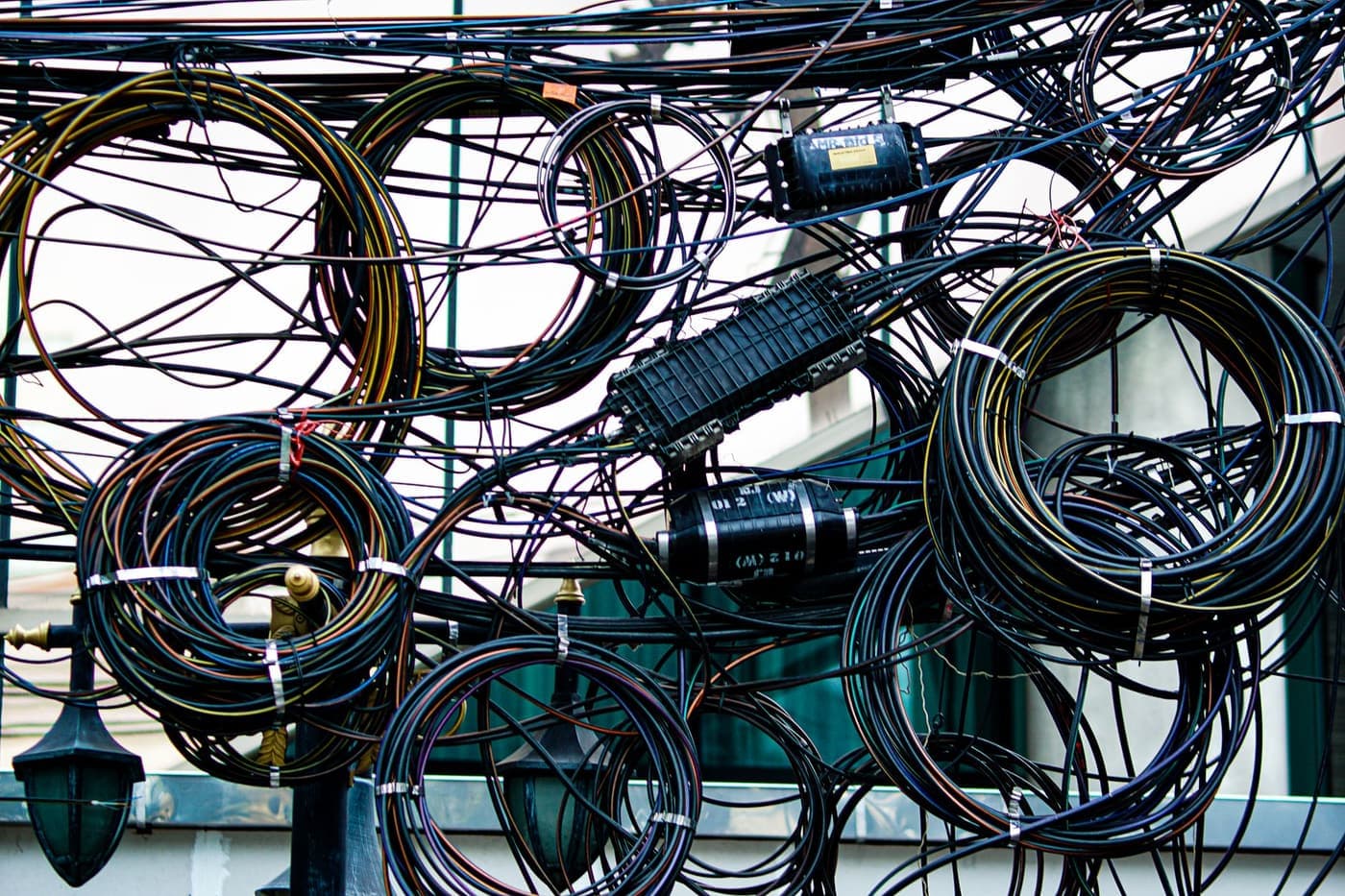 Tangle of overhead telecom cables and splice boxes above a street