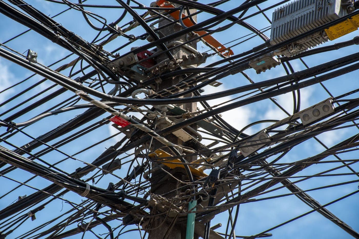 Utility pole tangled with overhead cables and wires against a blue sky
